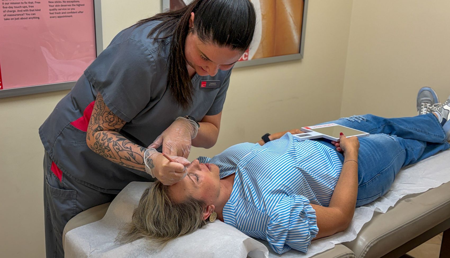Cassidy shaping a guest's brows while the guest holds a mirror